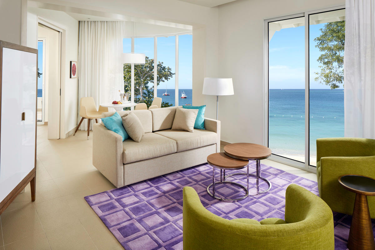 Resort suite with beige sofa, lime green chairs, and ocean views through floor-to-ceiling windows overlooking the beach.