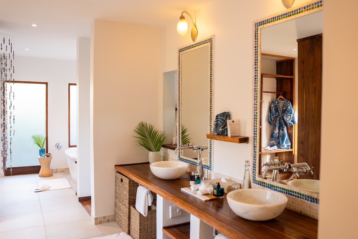 Spacious resort bathroom with dual vessel sinks on a wood countertop, tiled mirrors, potted plants, and a blue-tiled accent border.