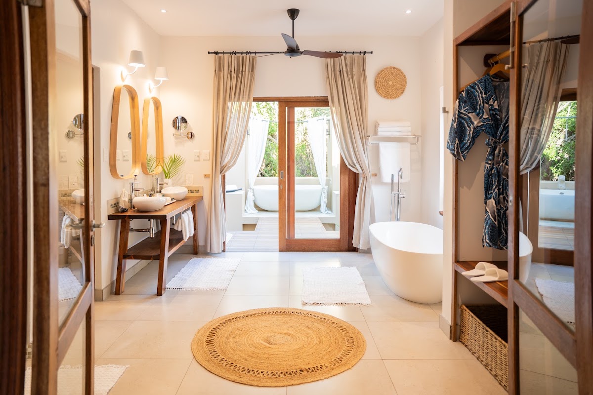Spacious resort bathroom with dual vanities, soaking tub, and wooden doors opening to outdoor shower area.
