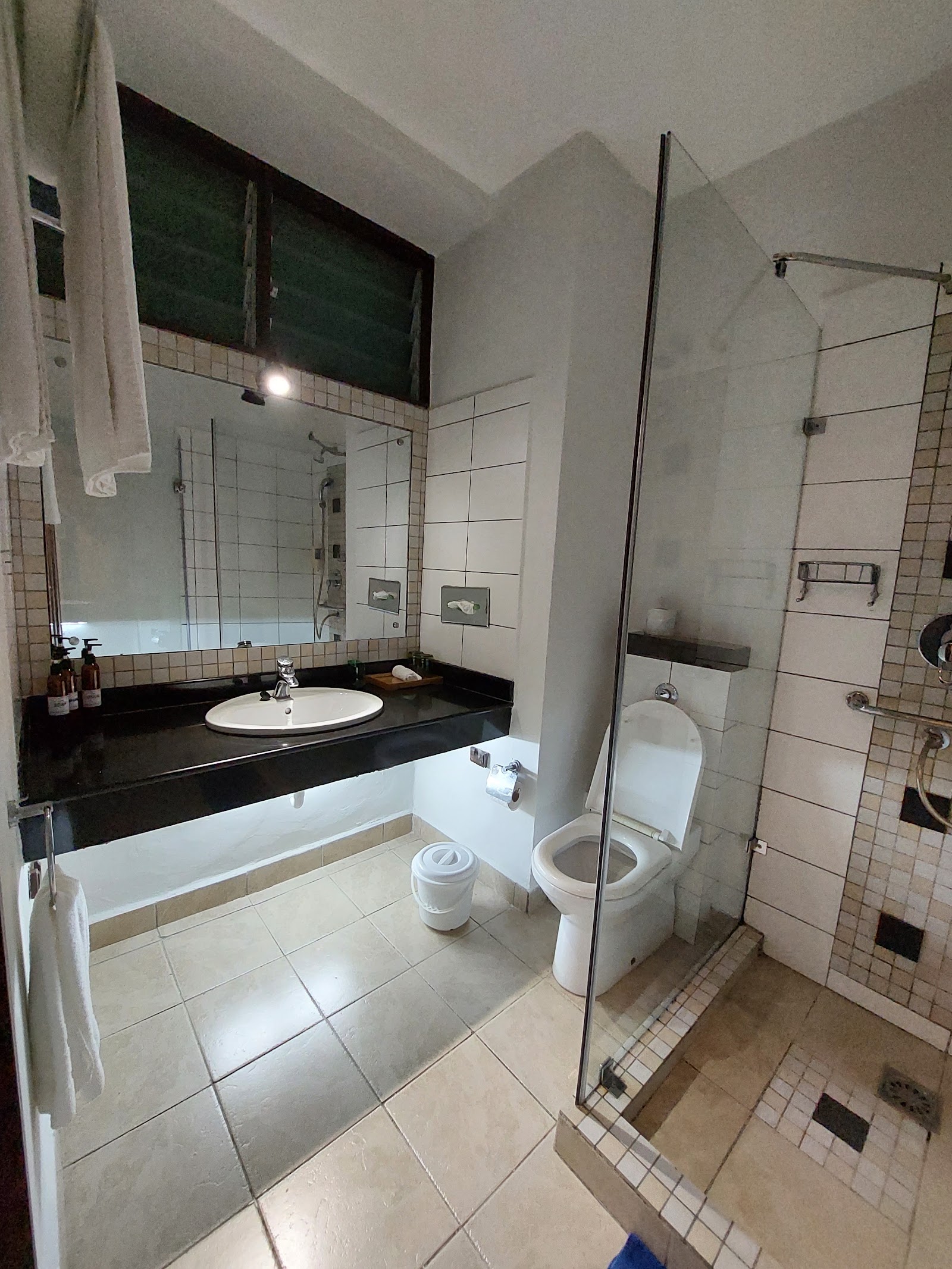 Resort bathroom with black countertop sink, white tile walls, bathtub, toilet, and glass-enclosed shower area.