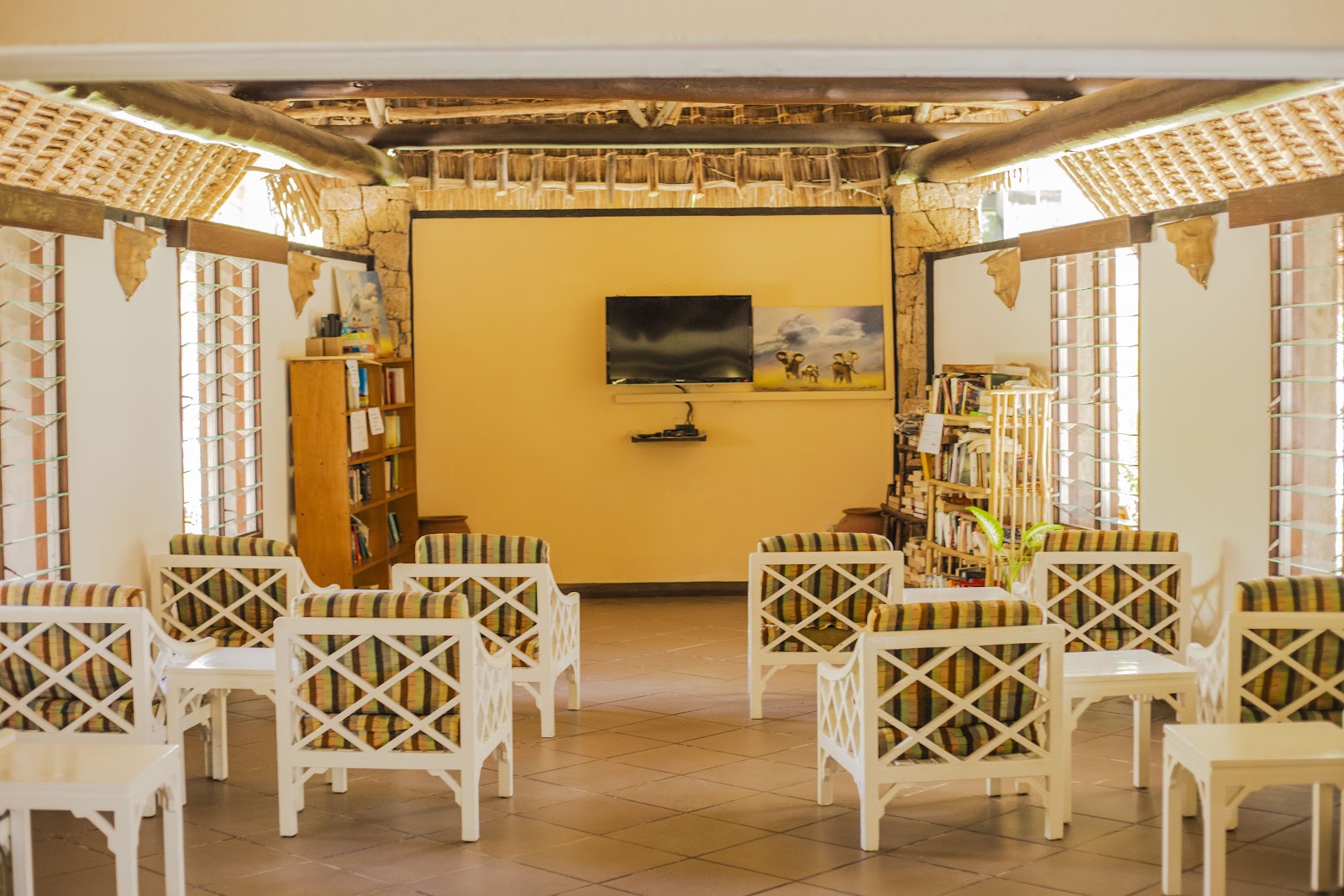 Open-air lounge with white wicker chairs, yellow walls, wooden beams, and bookshelves at Bahari Beach Hotel.