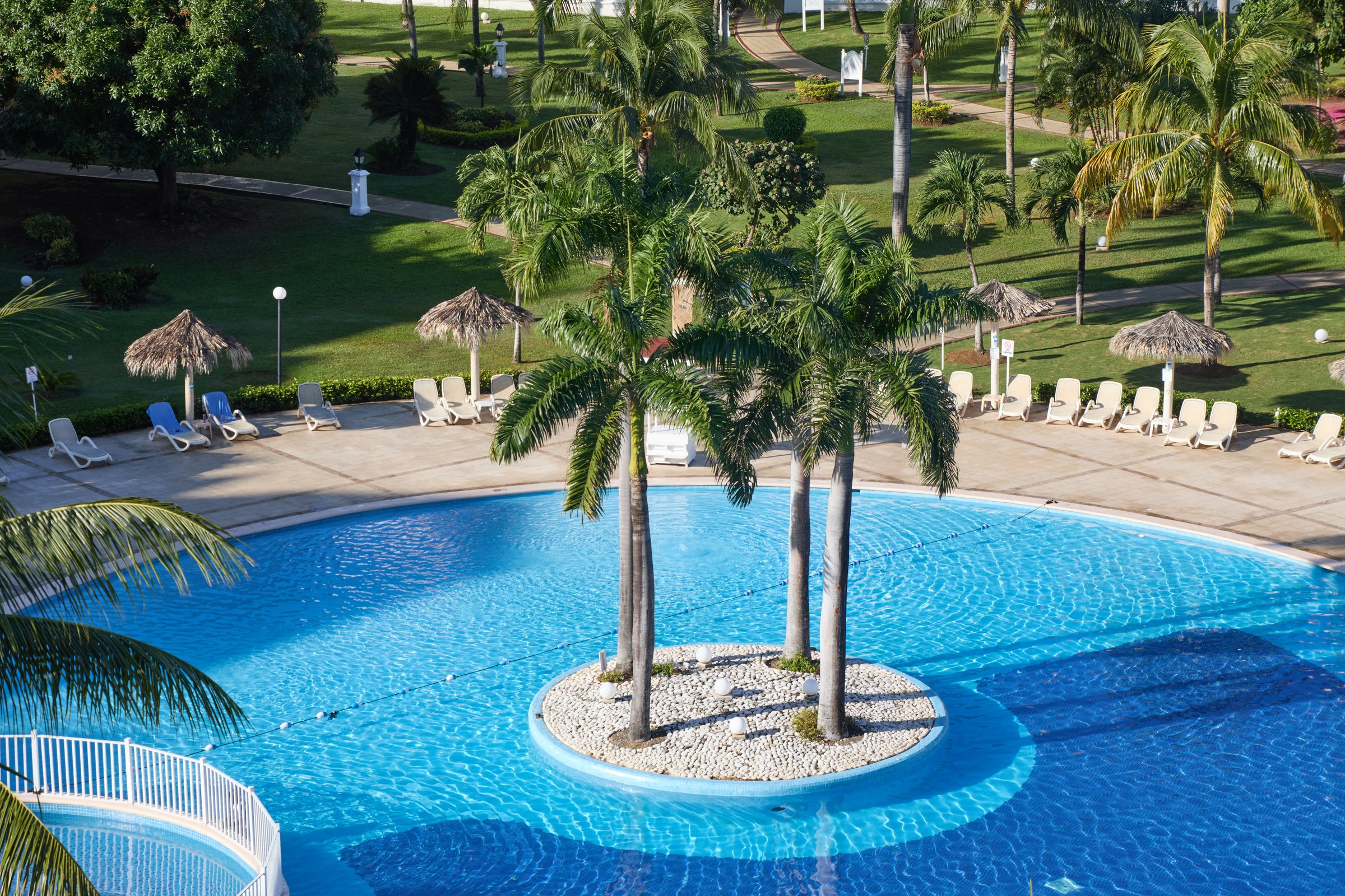 Circular pool with palm island and thatched umbrellas