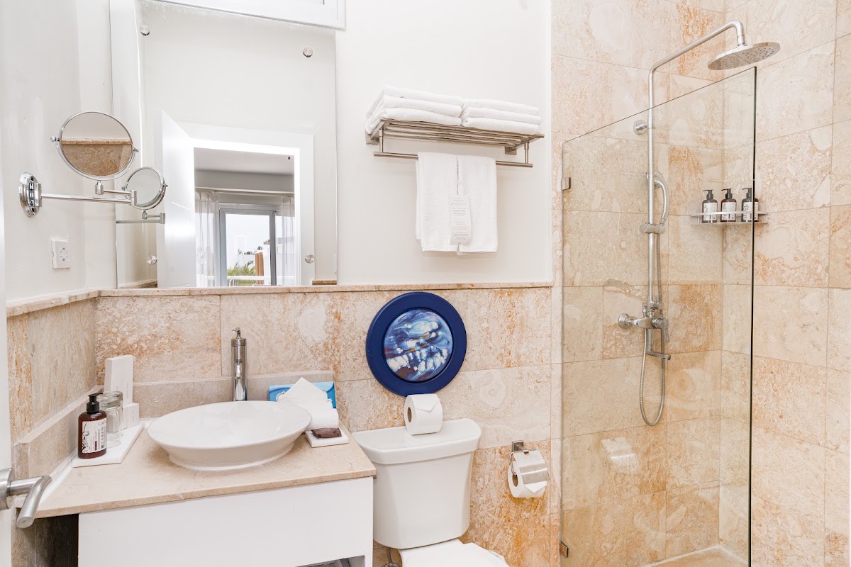 Bathroom with beige tile walls, white vessel sink, toilet, and glass-enclosed shower with rainfall showerhead at Bakour Punta Cana Suites.