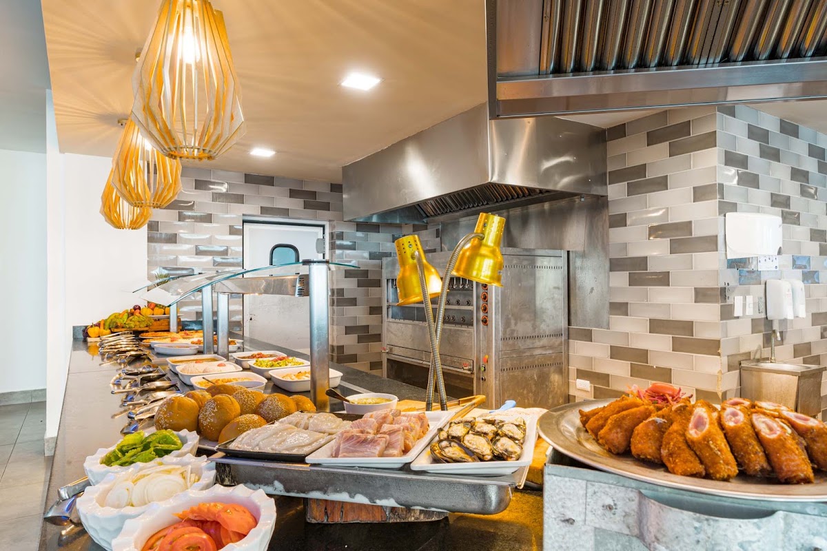 Bakour Punta Cana Suites buffet station displays fresh breads, meats, seafood, and prepared dishes under golden pendant lights and stainless steel hood.