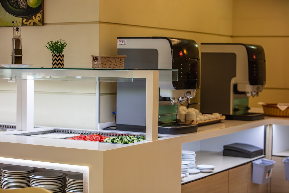 Resort buffet counter with salad bar, coffee machines, and plate storage under yellow walls.