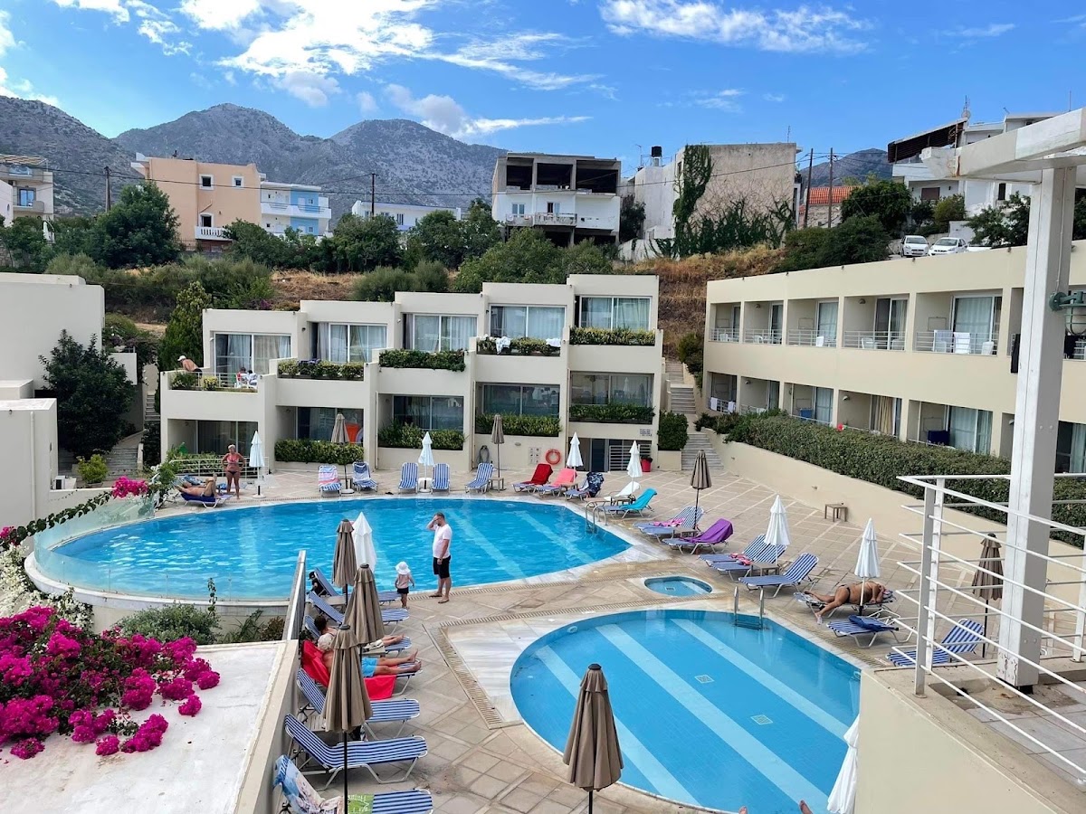 Bali Beach & Sofia Village Hotel pool area with two blue pools, striped loungers, umbrellas, and white buildings backed by rocky mountains.