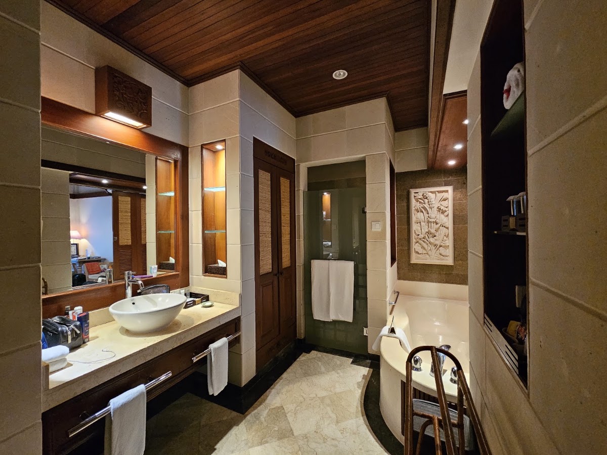 Bathroom with vessel sink on vanity, soaking tub, wood ceiling, and neutral tile walls at Bali Tropic Resort & Spa.