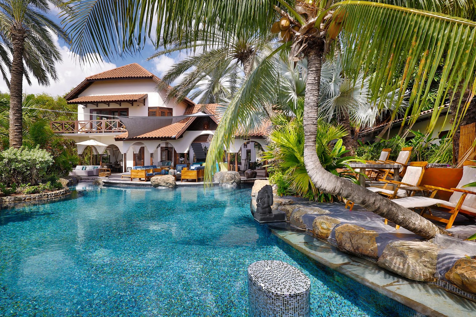 Baoase Luxury Resort's turquoise pool surrounded by palm trees, loungers, and a white villa with terracotta roof overlooking the water.