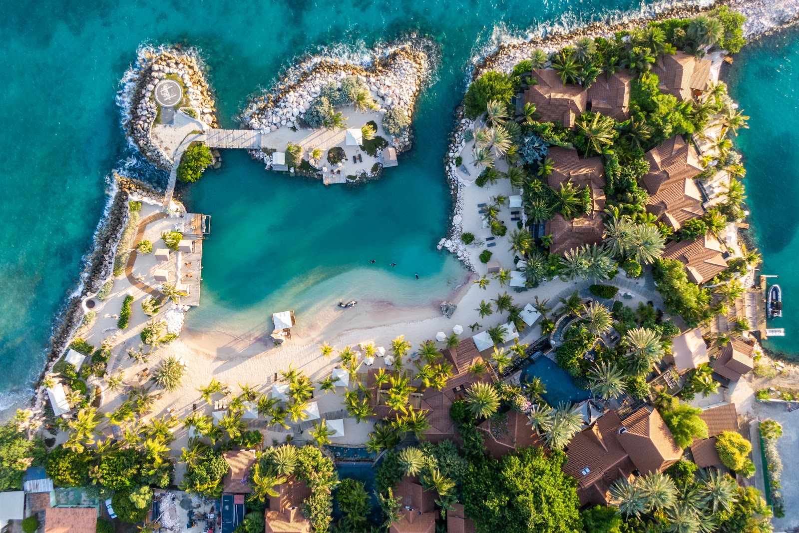 Aerial view of Baoase Luxury Resort's private beach cove with turquoise water, white sand, thatched bungalows, and rocky outcrops surrounding the lagoon.