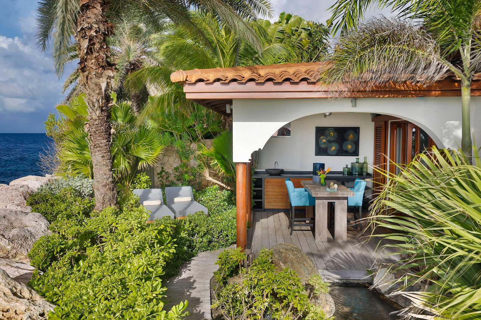Beachfront bungalow at Baoase Luxury Resort with curved architecture, thatched roof, and ocean view beyond palm trees and tropical vegetation.