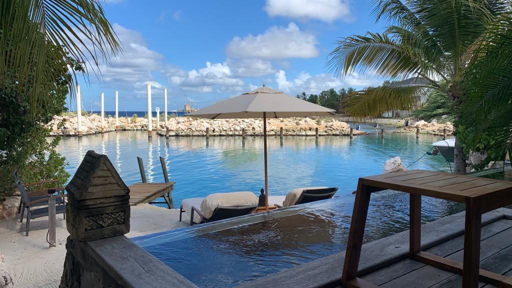Wooden deck with lounge chairs overlooks turquoise water, rocky outcrops, and sandy beach at Baoase Luxury Resort.
