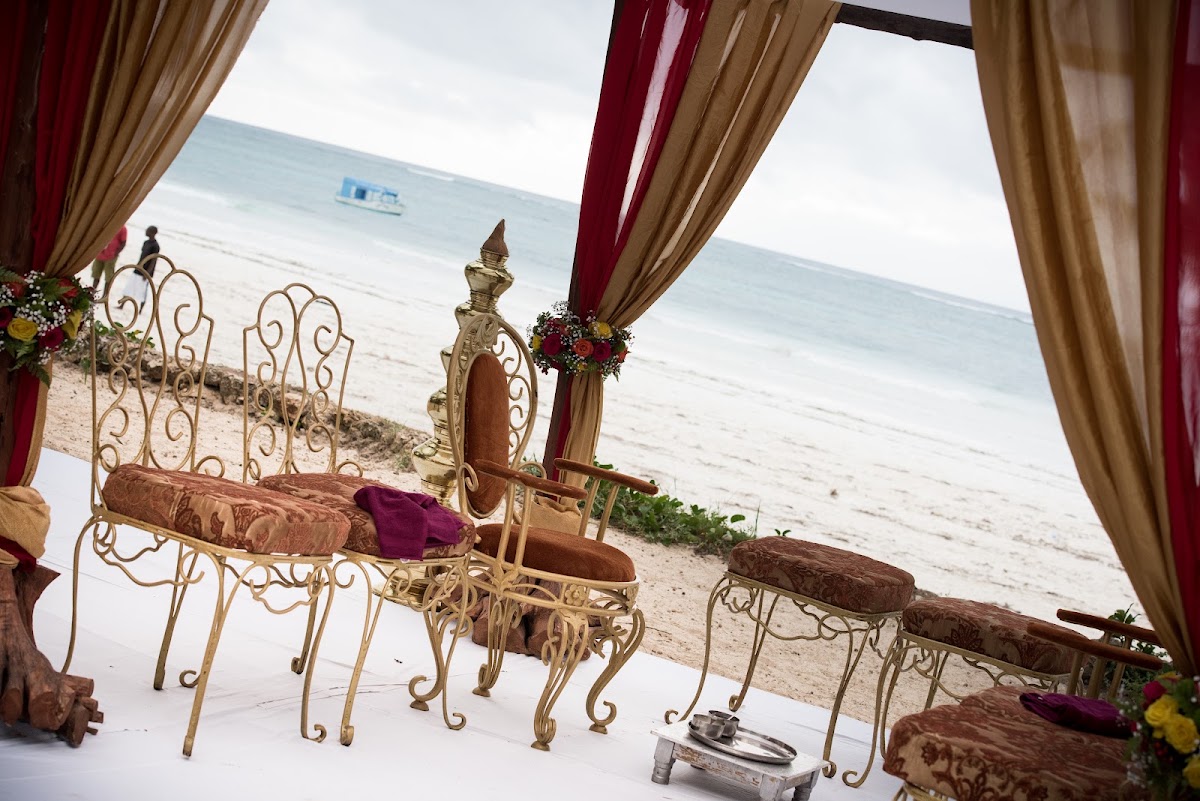 Ornate gold chairs and decorative mirror with burgundy and tan drapes frame a beach ceremony setup overlooking the ocean at Baobab Beach Resort & Spa.