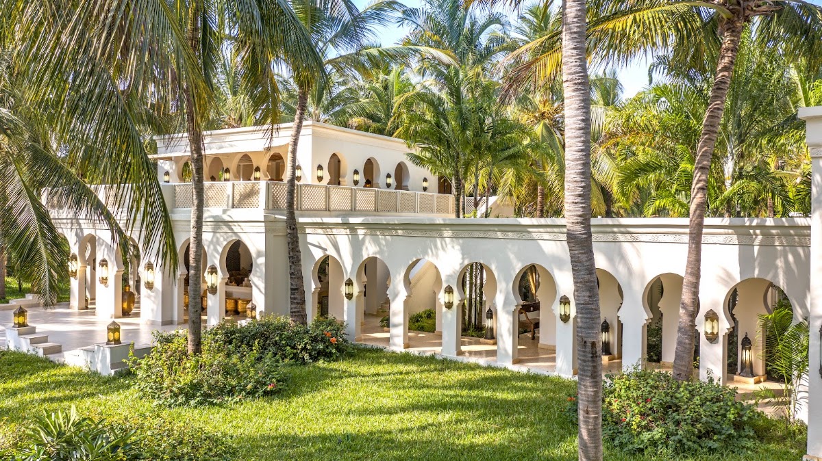 White Moorish-style building with arched openings and upper balcony surrounded by tall palm trees and manicured lawn at Baraza Resort & Spa.