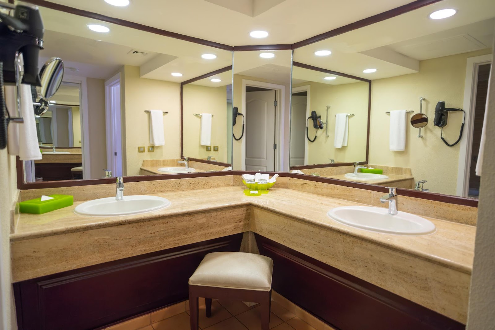 Large shared bathroom with dual vanities, framed mirrors, travertine countertops, and a makeup stool at the center.