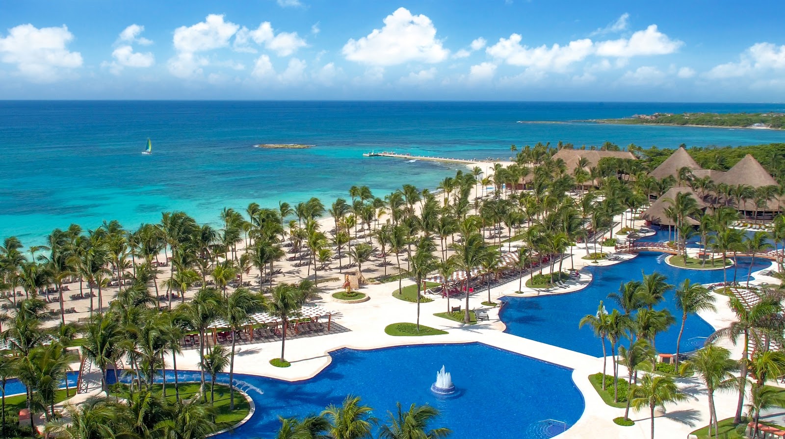 Aerial view of Barceló Maya Colonial with curved blue pools, palm-lined white beach, and turquoise Caribbean Sea beyond.