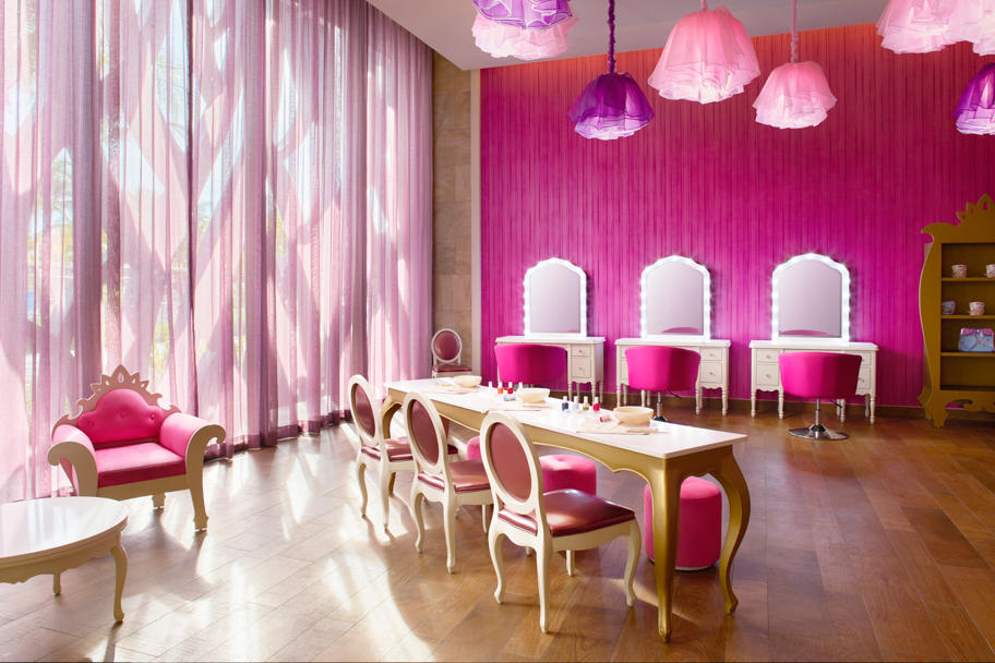 Spa salon with bright pink walls, ornate wooden vanity stations with mirrors, pink pendant lamps, and cream and pink chairs at the Barceló Maya Grand Resort.