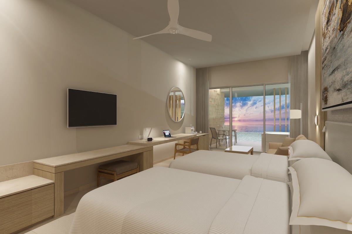 Resort bedroom with two beds, desk, TV, and ocean view through floor-to-ceiling windows at sunset.