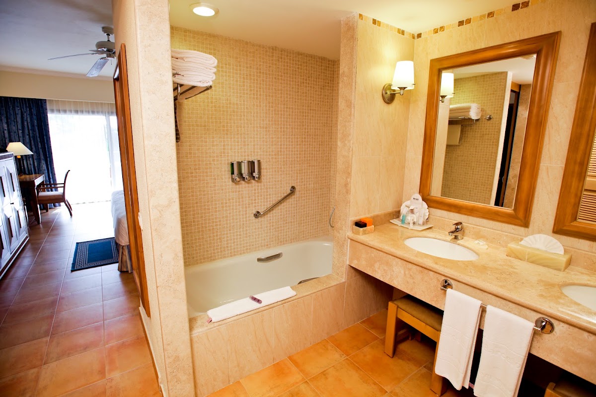 Bathroom with tiled shower-tub combo, wooden vanity with round sink, large mirror, and folded towels on shelving.
