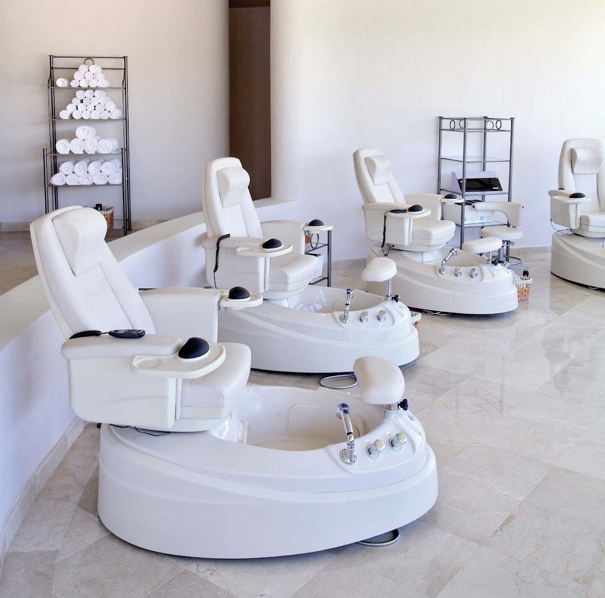 Spa pedicure station with white massage chairs, foot basins, and rolled towels stacked on shelving at Barceló Maya Tropical.