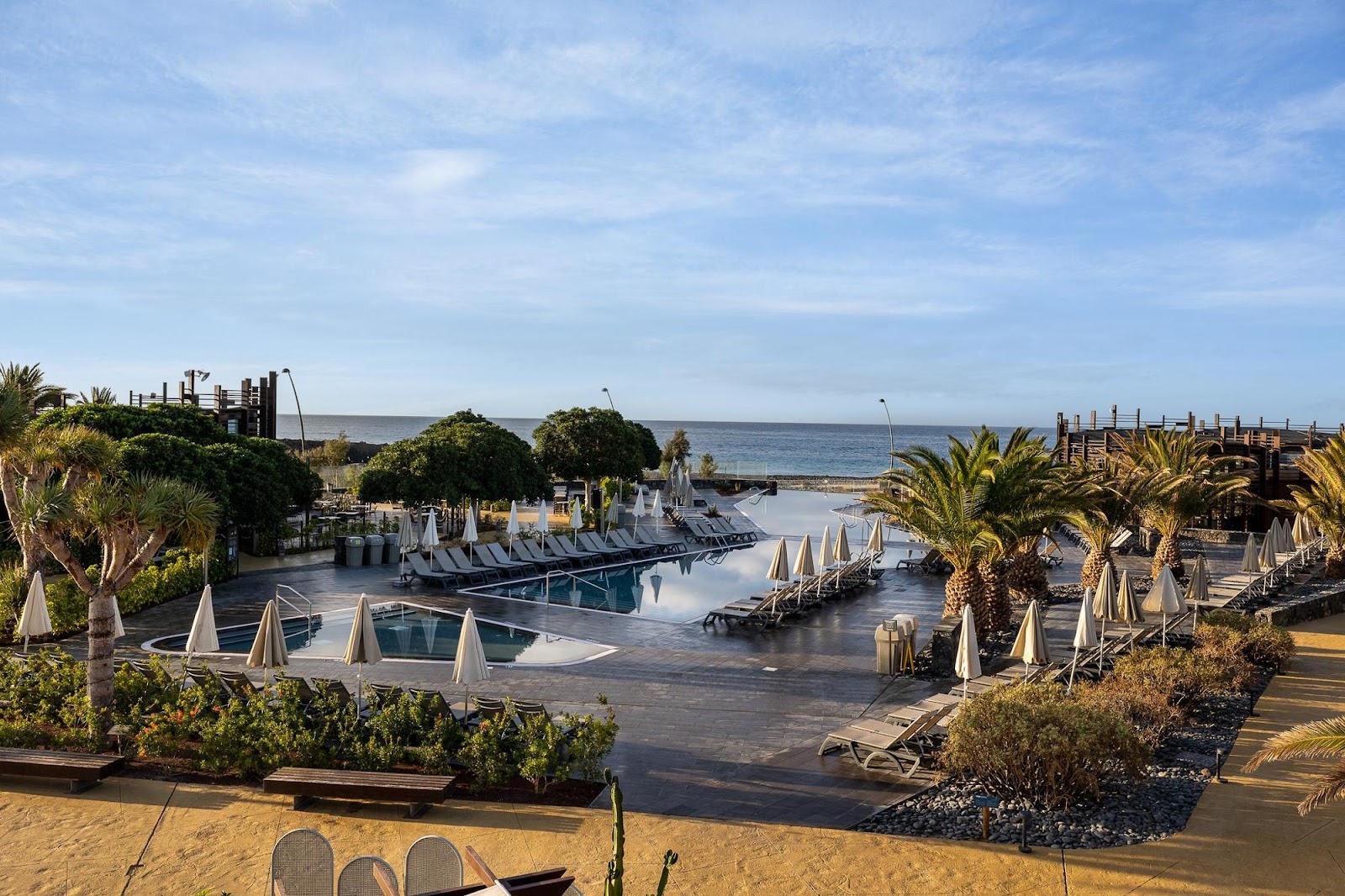 Pool area with loungers and umbrellas at Barceló Tenerife, overlooking the ocean and palm trees under clear sky.