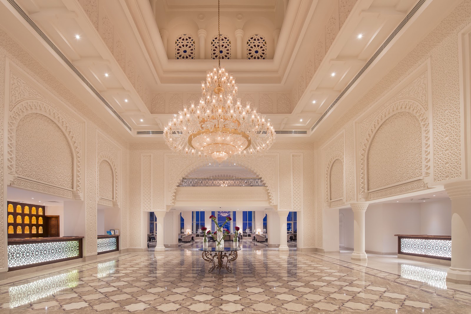 Grand lobby of Baron Palace Sahl Hasheesh with ornate cream-colored walls, large crystal chandelier, and arched columns leading to ocean views.