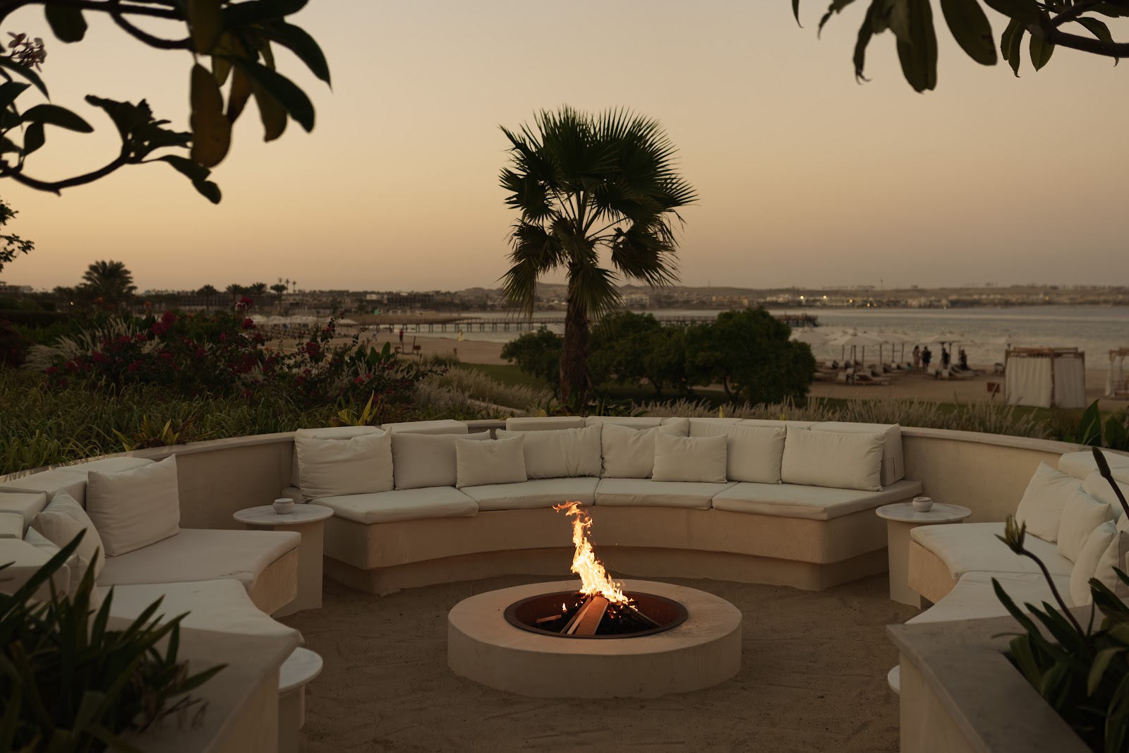 Resort suite interior with views through glass doors to pool, lawn, and white Mediterranean-style building with palm trees.