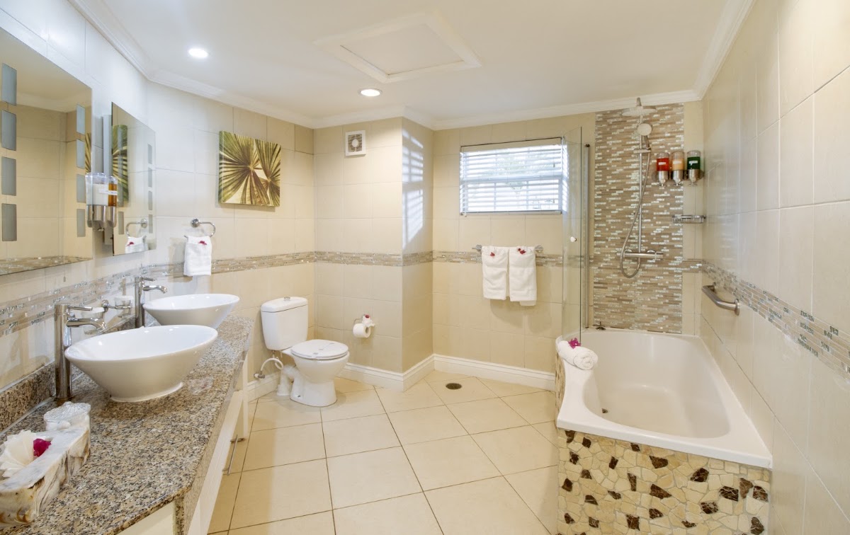 Spacious bathroom at Bay Gardens Beach Resort & Spa with dual sinks, soaking tub, separate shower enclosure, and cream tile flooring.