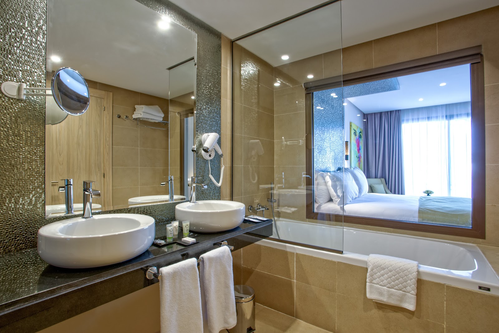 Modern bathroom with dual round sinks, glass shower enclosure, and mirrored wall overlooking a bedroom at Be Live Collection Marrakech Adults Only.