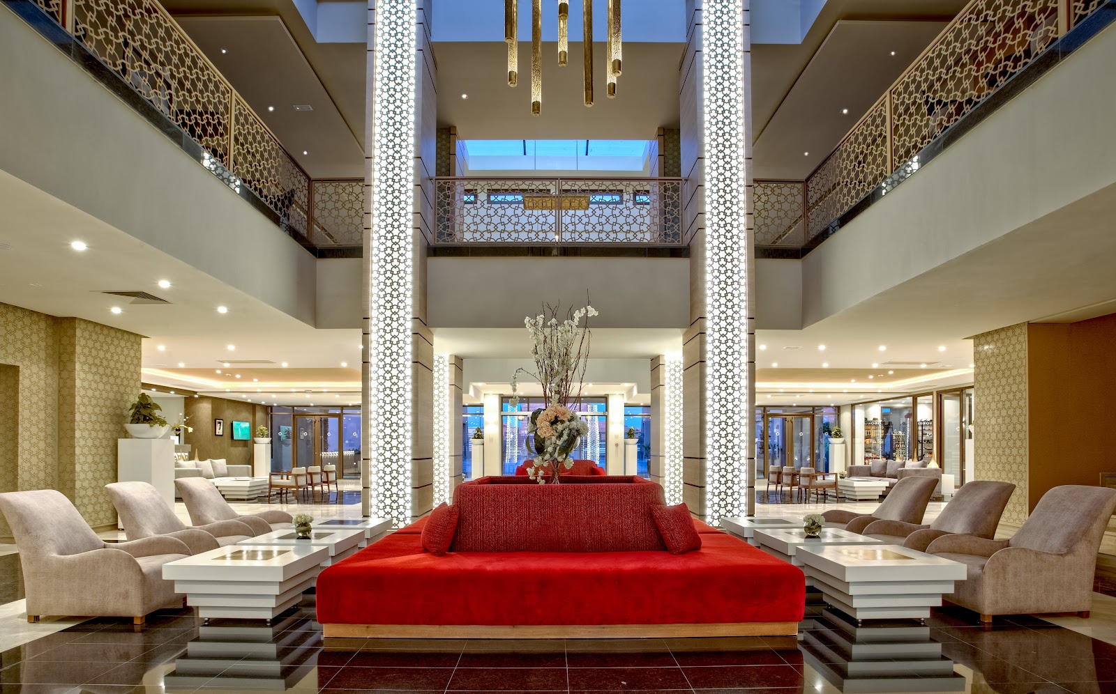 Symmetrical resort lobby with a central red sofa, geometric white columns, beige armchairs on either side, and skylights overhead at Be Live Collection Marrakech Adults Only.