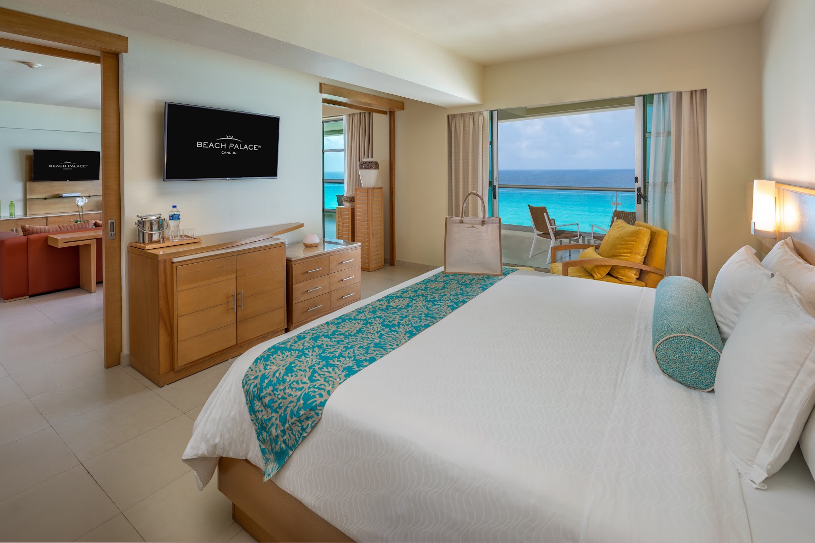 Oceanfront resort bedroom with king bed, soaking tub in foreground, and turquoise sea visible through balcony doors.