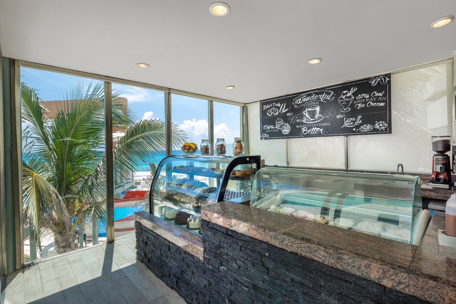 Beach Palace coffee shop interior with display cases, ocean and palm trees visible through large windows.