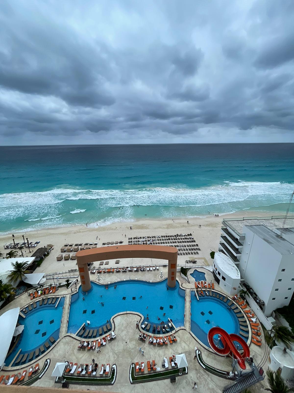 Resort pool with curved archway and lounge chairs overlooking the beach, turquoise ocean, and stormy sky at Beach Palace.