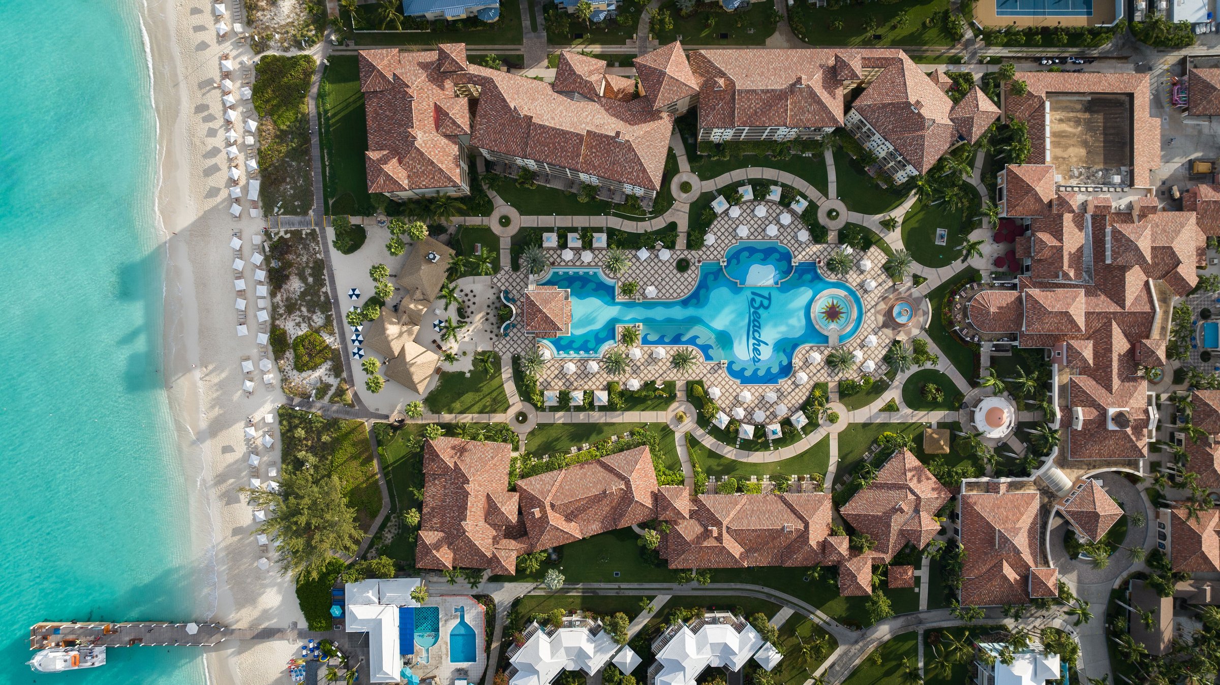 Top-down aerial of the Italian Village pool between terracotta roofs and the beach.