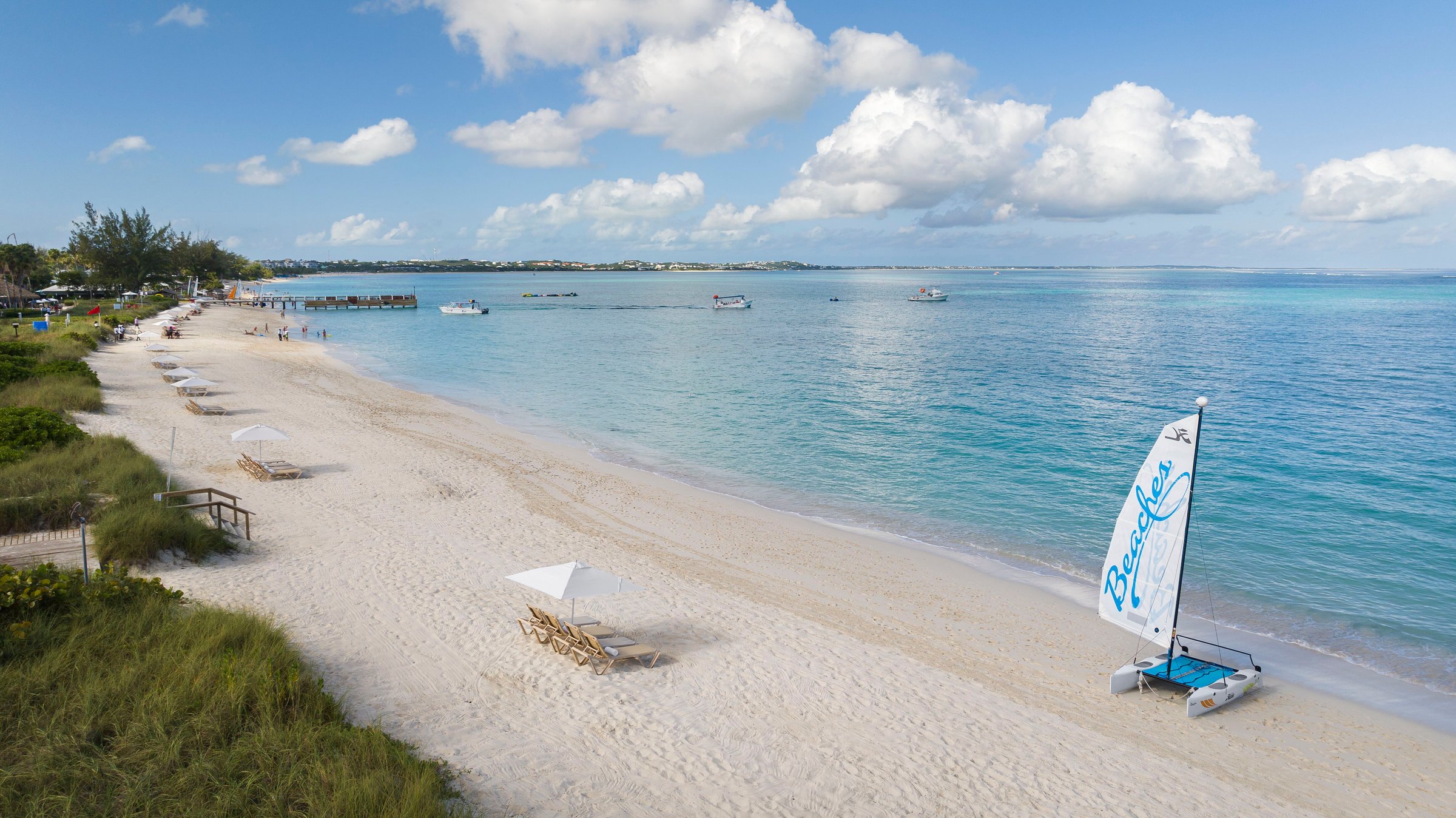 Beaches-branded catamaran on the long white-sand beach of Grace Bay with calm turquoise water.
