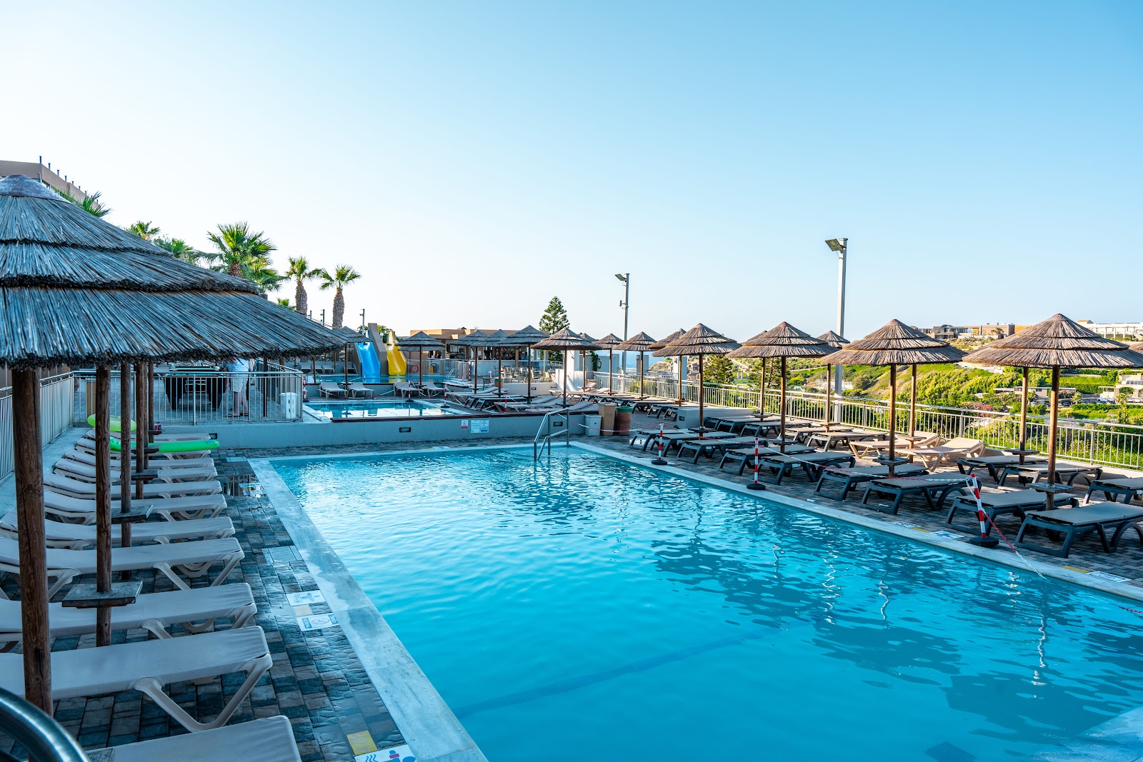 Blue Bay Resort Hotel's main pool with lounge chairs, thatched umbrellas, and palm trees under clear sky.