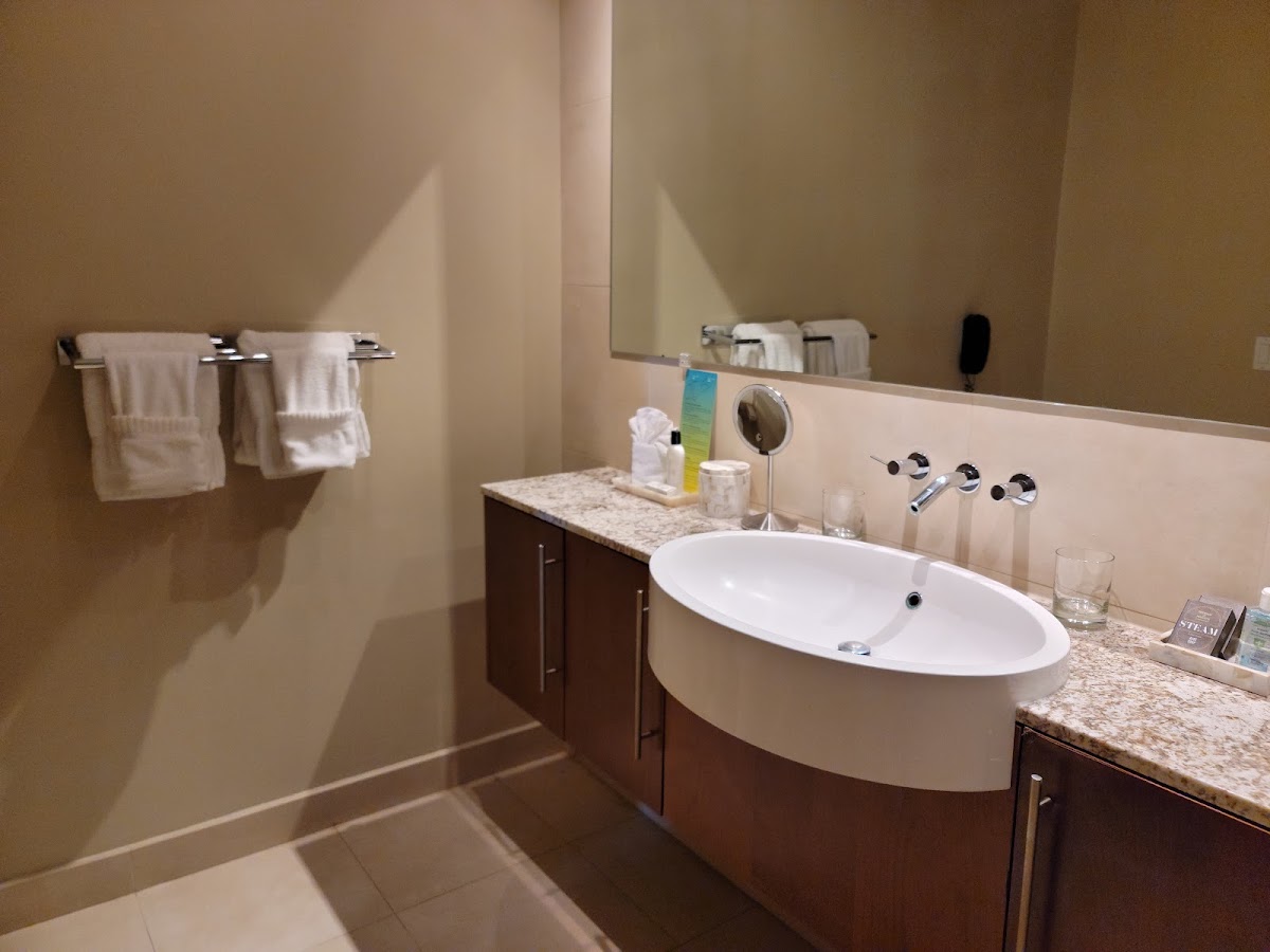 Resort bathroom with curved white sink, granite countertop, dark wood vanity, and white towels on rack.