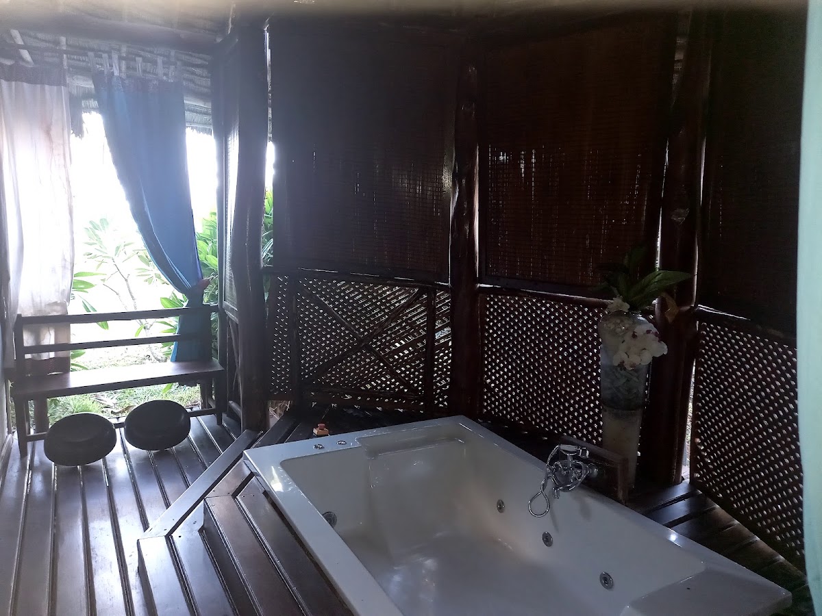 Private open-air bathroom with soaking tub, latticed wooden walls, and tropical plants visible through the entrance.