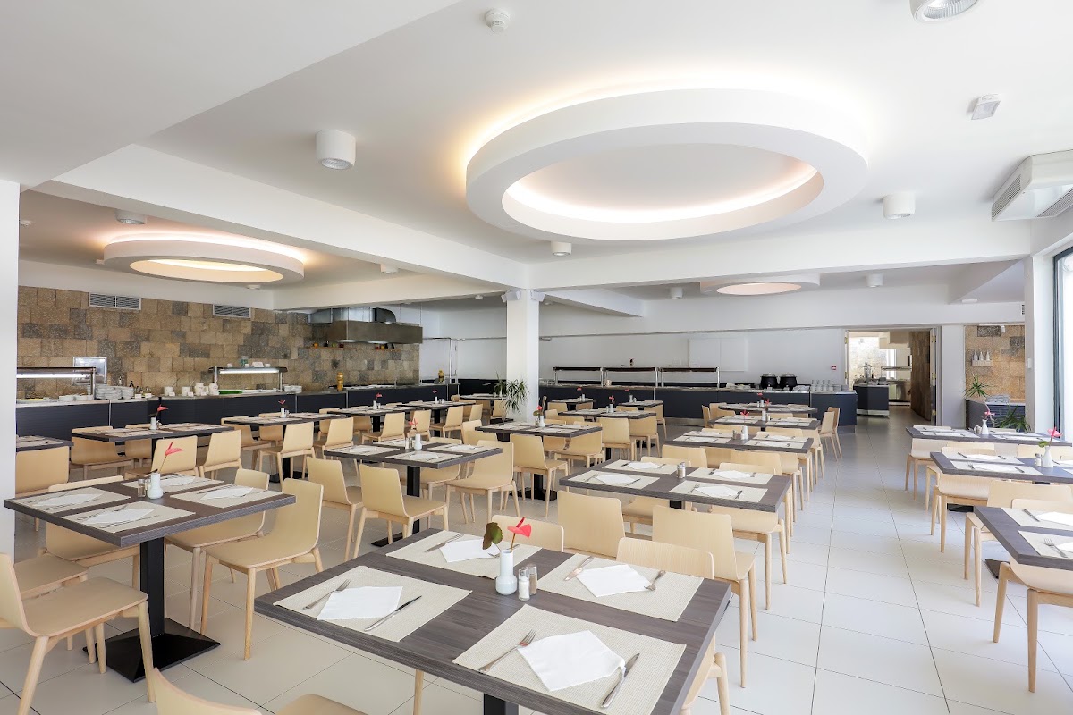 Spacious dining room with beige chairs, dark tables set with place settings, and recessed ceiling lights at Bluesun Hotel Neptun.