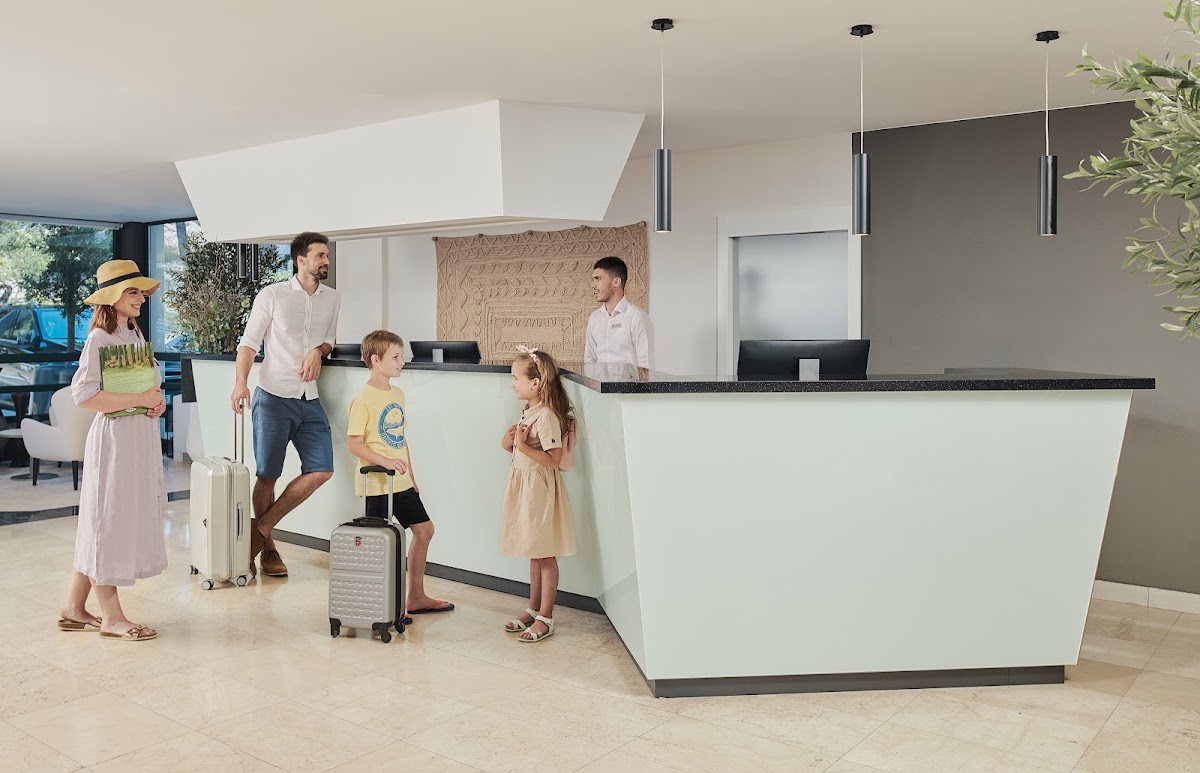 Family checking in at a modern reception desk with luggage, staff member assisting at the counter.