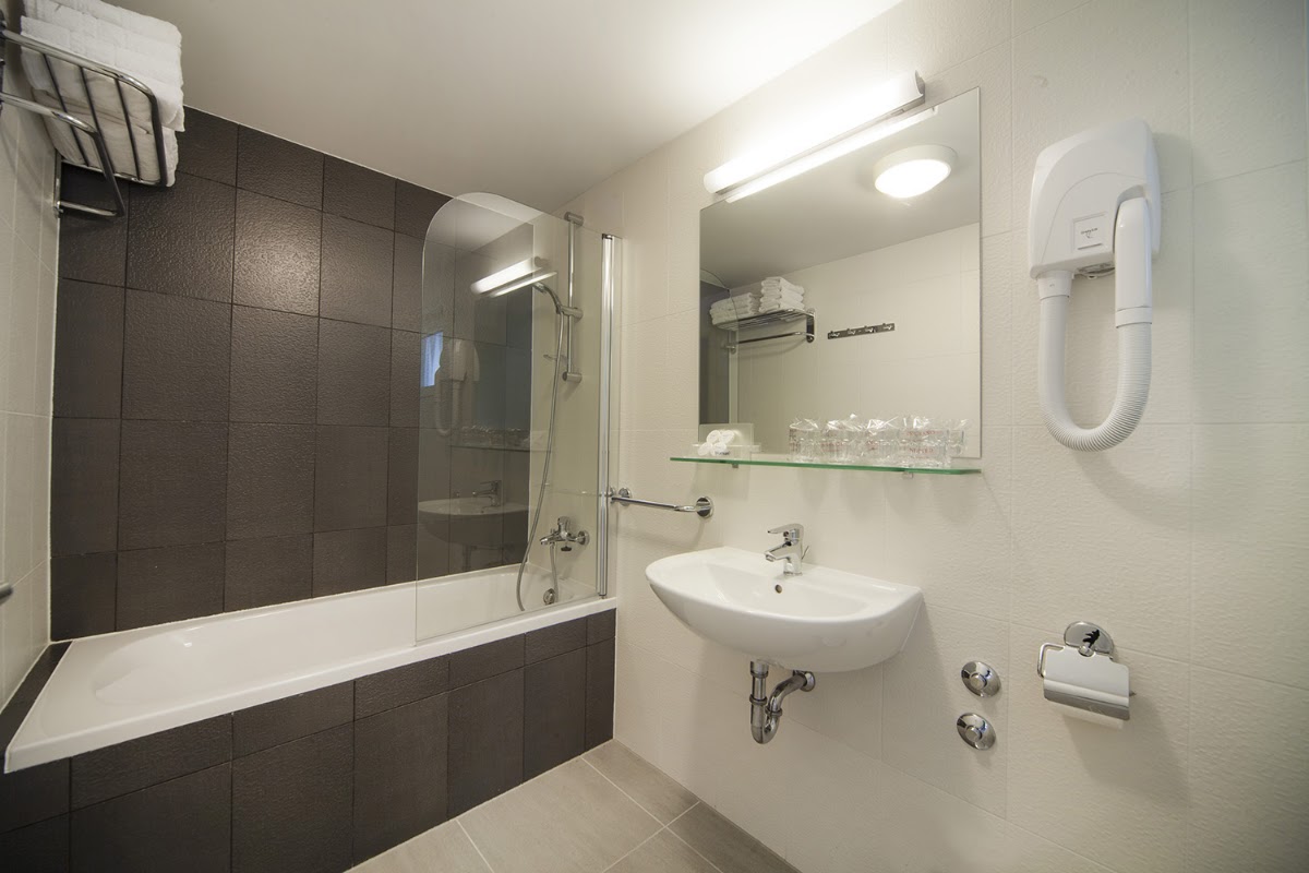 Modern bathroom with dark tile shower enclosure, white sink, large mirror, and folded towels on wall rack.