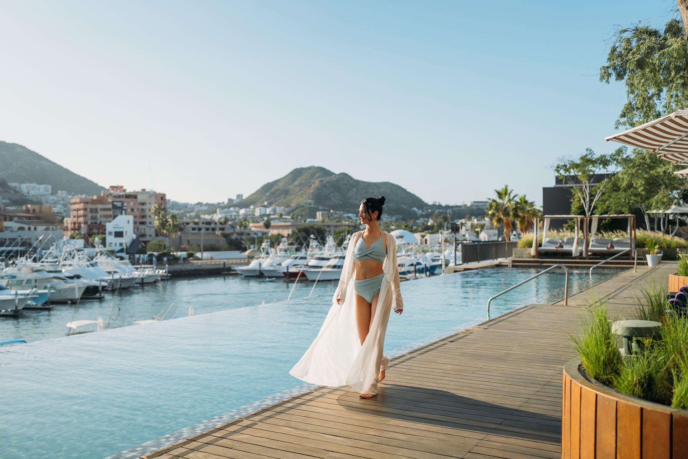 Wooden pool deck beside the infinity pool with the marina and mountains behind.