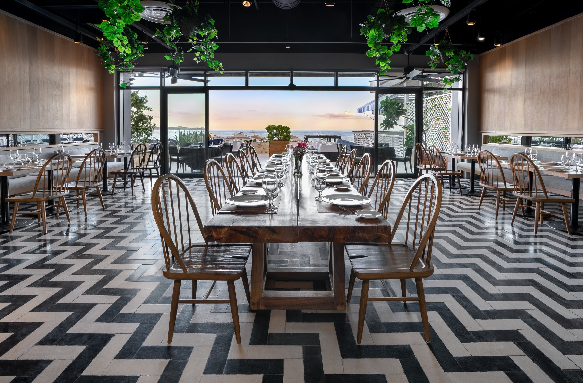 Spumante dining room with a long wooden table, black and white chevron floor, hanging greenery and glass doors to the terrace.