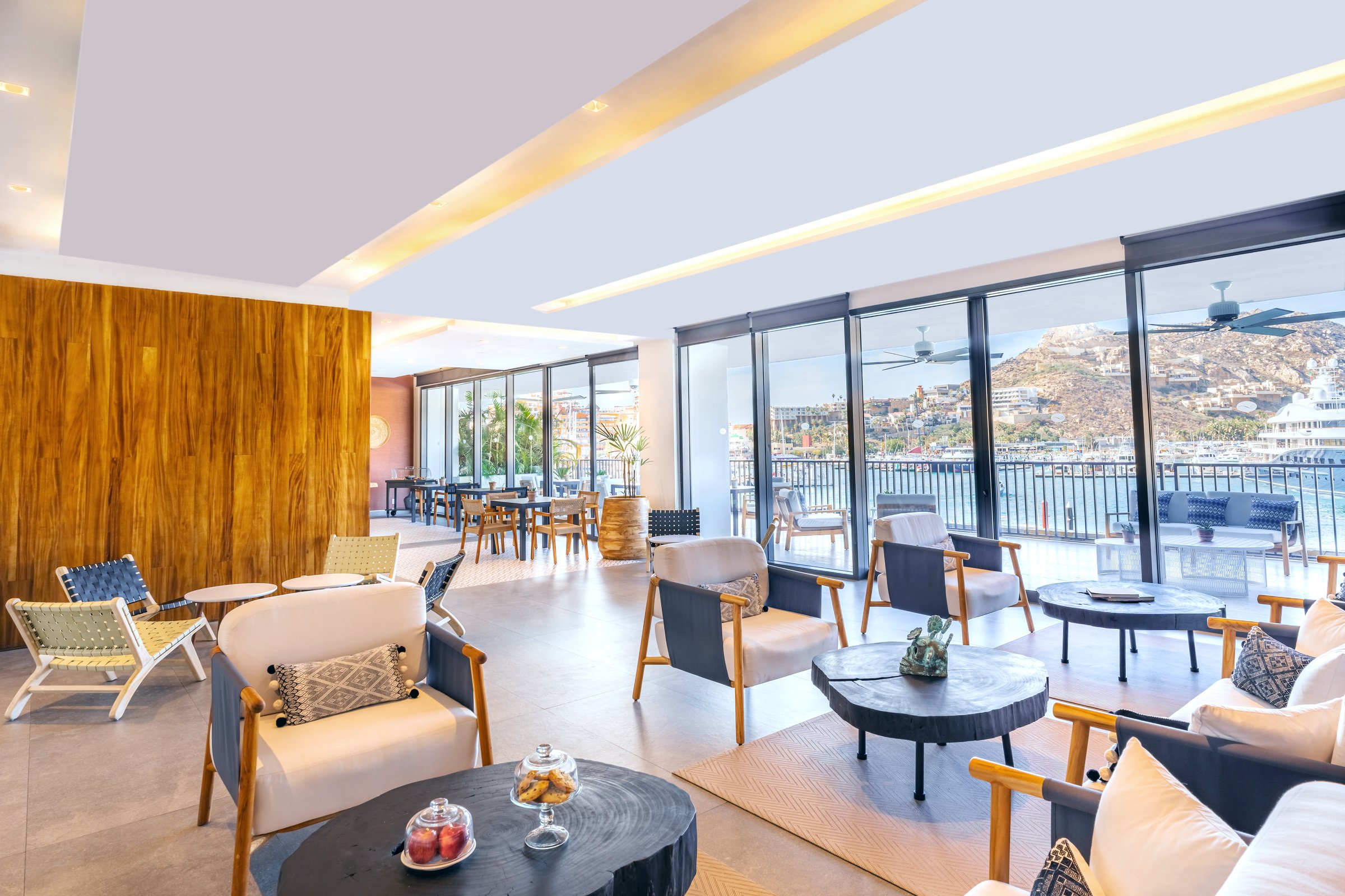 Xhale Club lounge seating area with modern armchairs, wood wall paneling and an opening to a balcony over the marina and mountains.