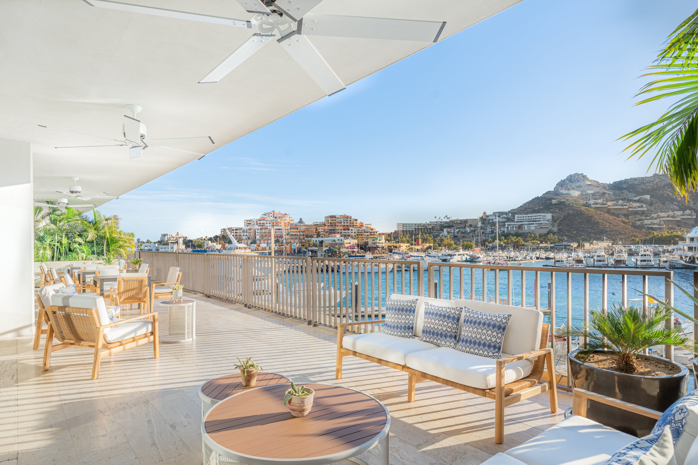 Xhale Club patio lounge with white wooden furniture and light blue pillows overlooking the marina and hills.