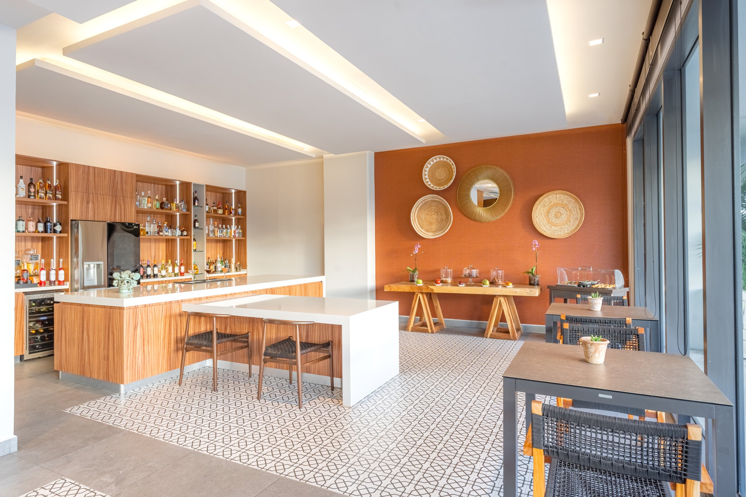 Xhale Club exclusive lounge bar with light wood cabinetry, a white marble counter and an orange accent wall hung with woven plates.
