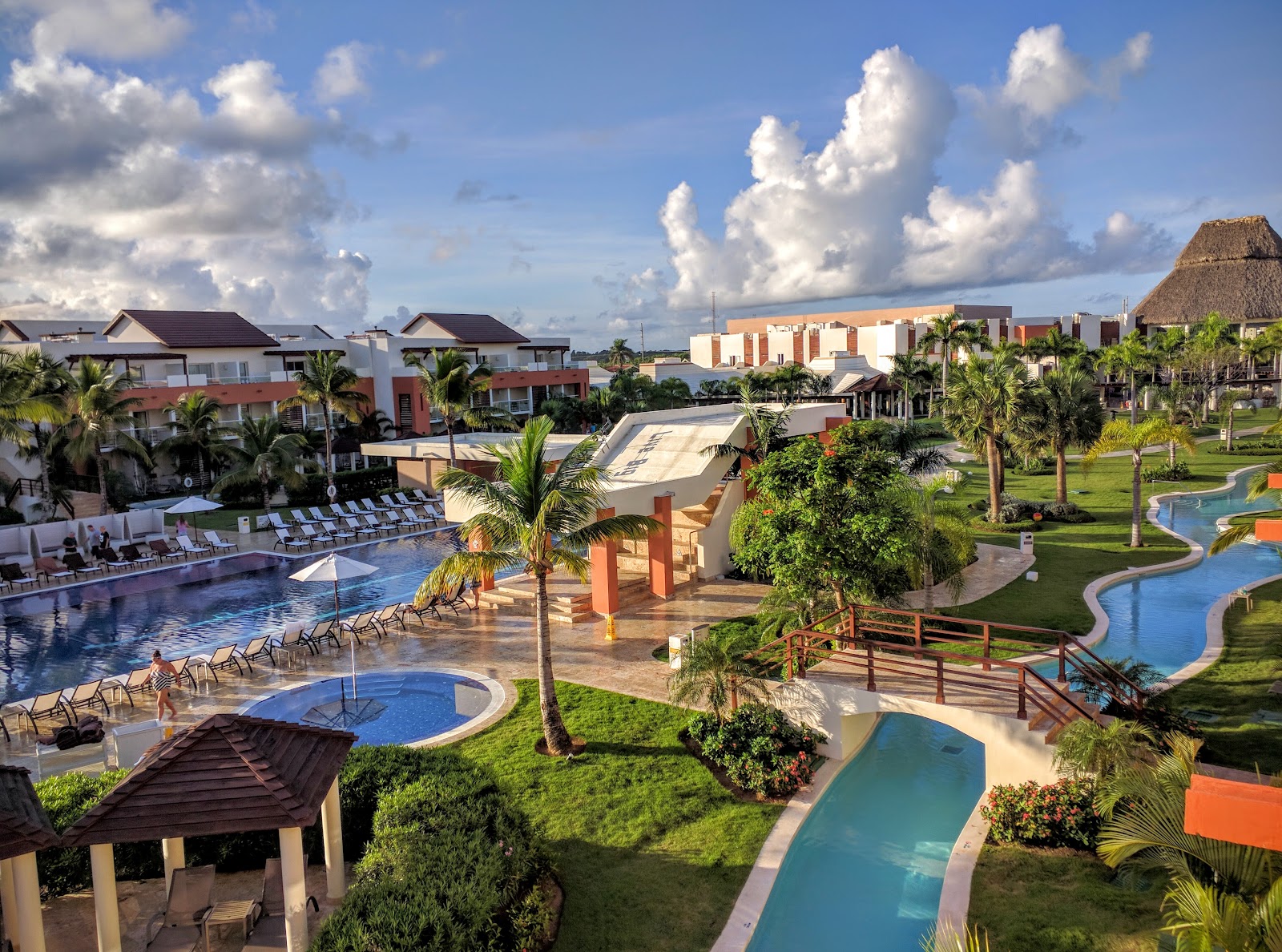 Breathless Punta Cana Resort & Spa grounds with multiple swimming pools, palm trees, loungers, and red-roofed buildings under a blue sky with white clouds.