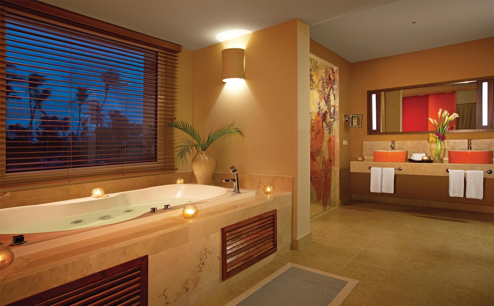Spa bathroom with soaking tub, dual vanities with red vessel sinks, and ocean views through louvered windows at dusk.