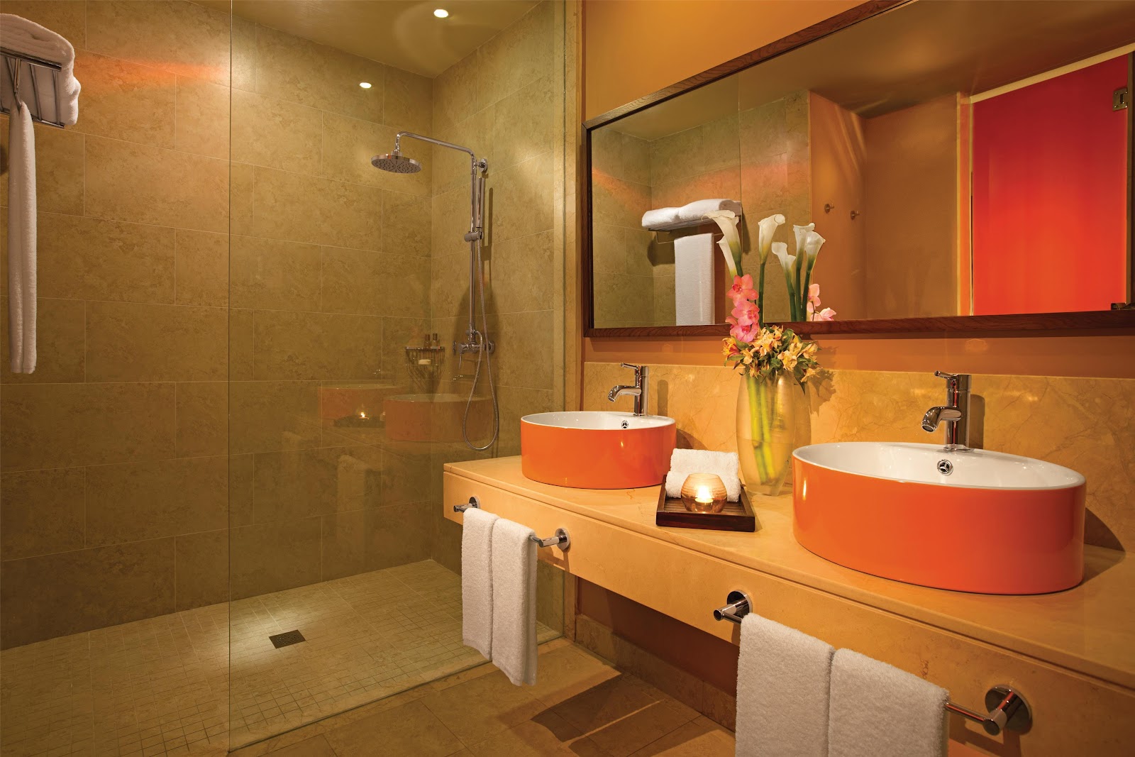 Modern resort bathroom with dual orange vessel sinks, walk-in shower, and fresh flowers on marble countertop.