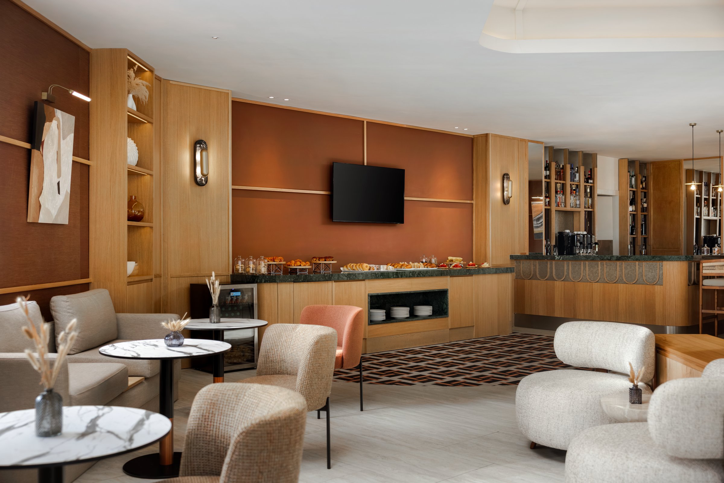 Xhale Club lounge area with light-wood shelving, a terracotta accent wall and white rounded chairs by a small food counter.