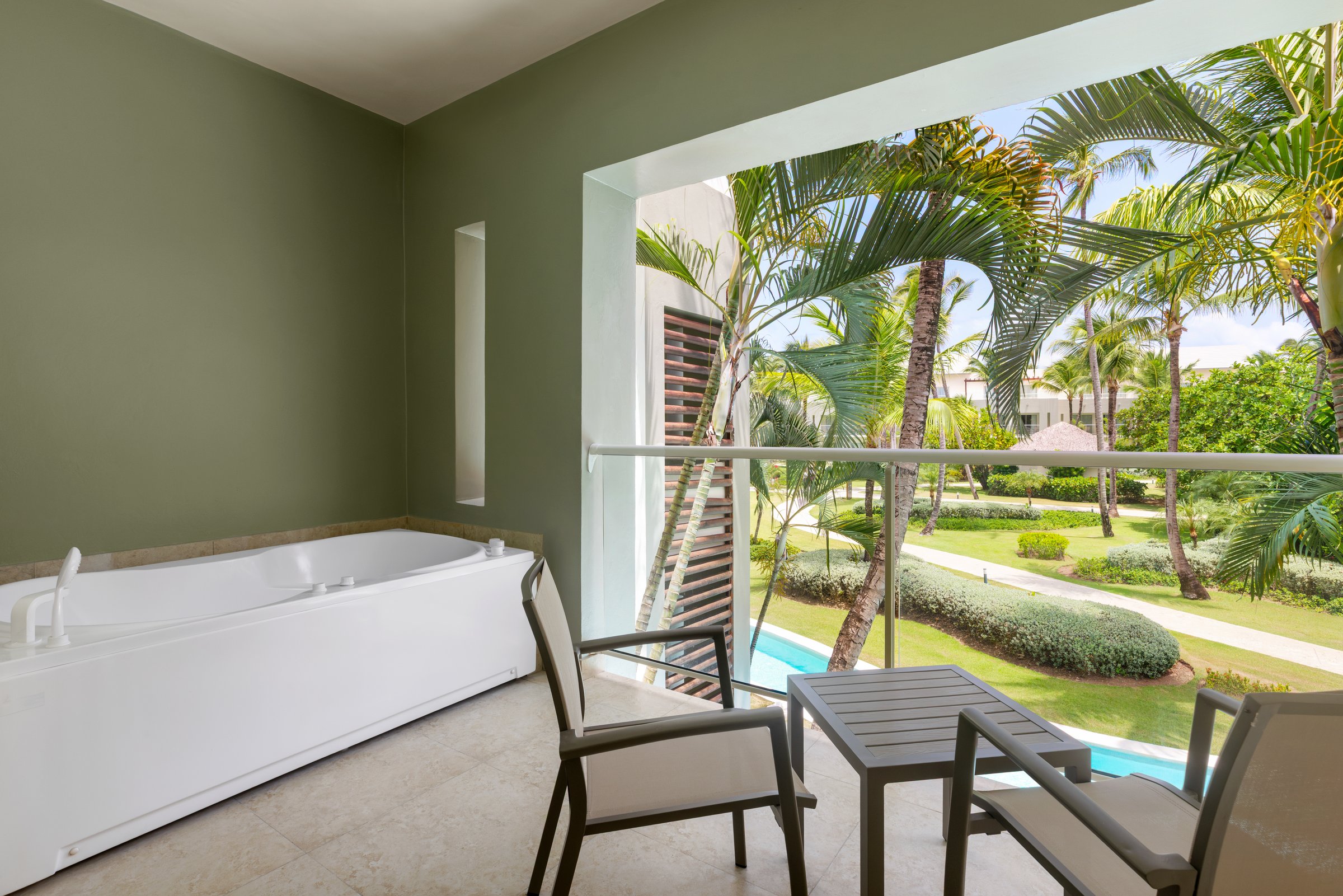 Allure suite terrace with a white built-in whirlpool, a grey table and chairs, over a manicured garden with palms.
